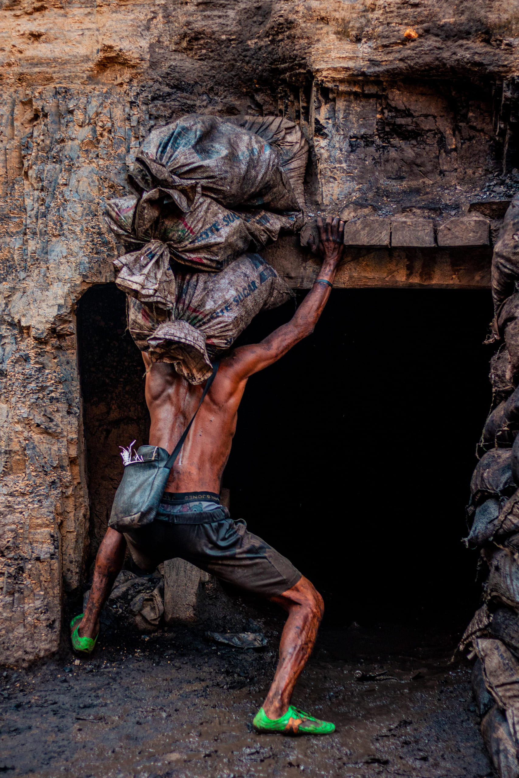 A charcoal worker climbing out of the dark opening of a kiln.