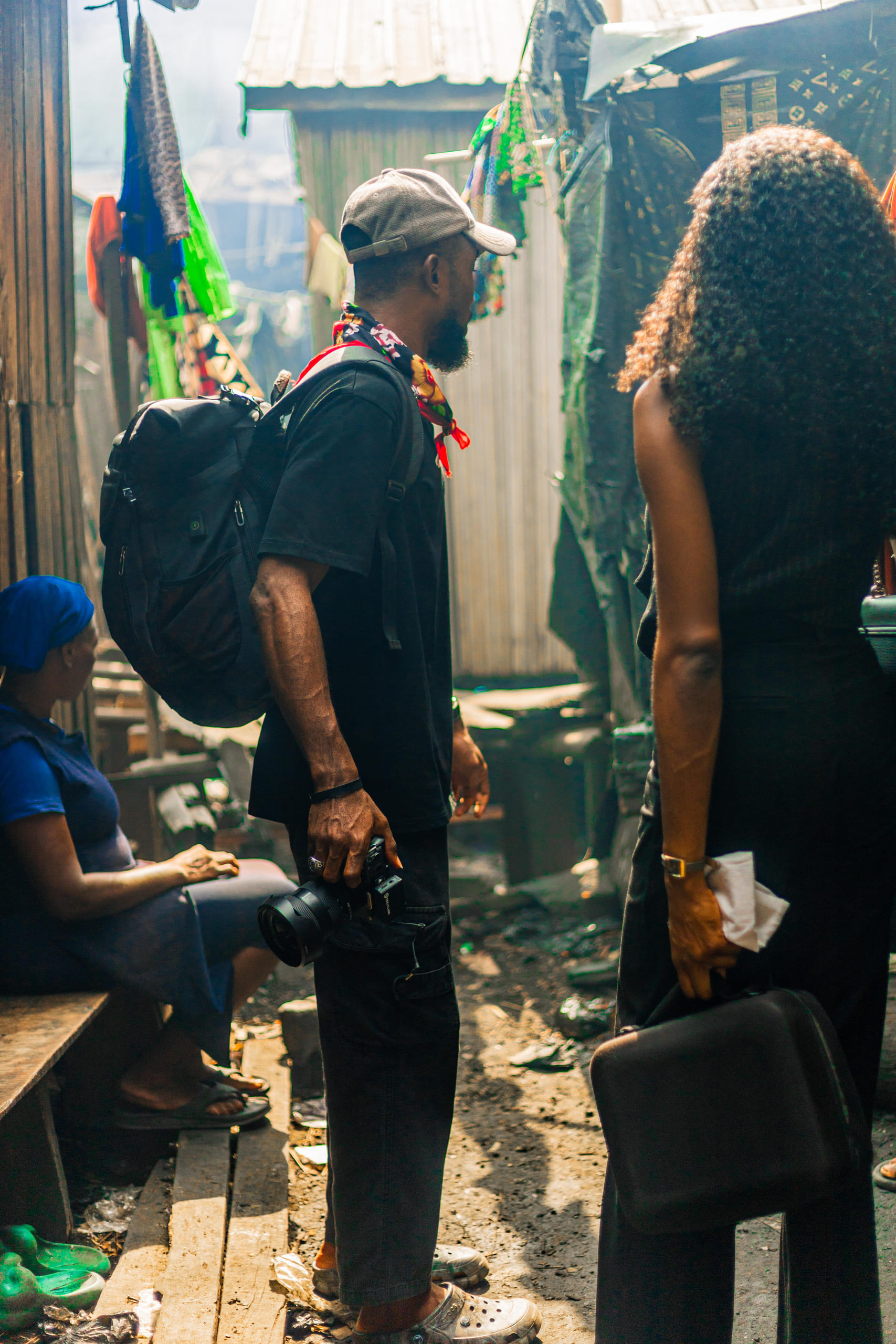 A crew member carrying a backpack through a narrow settlement walkway.